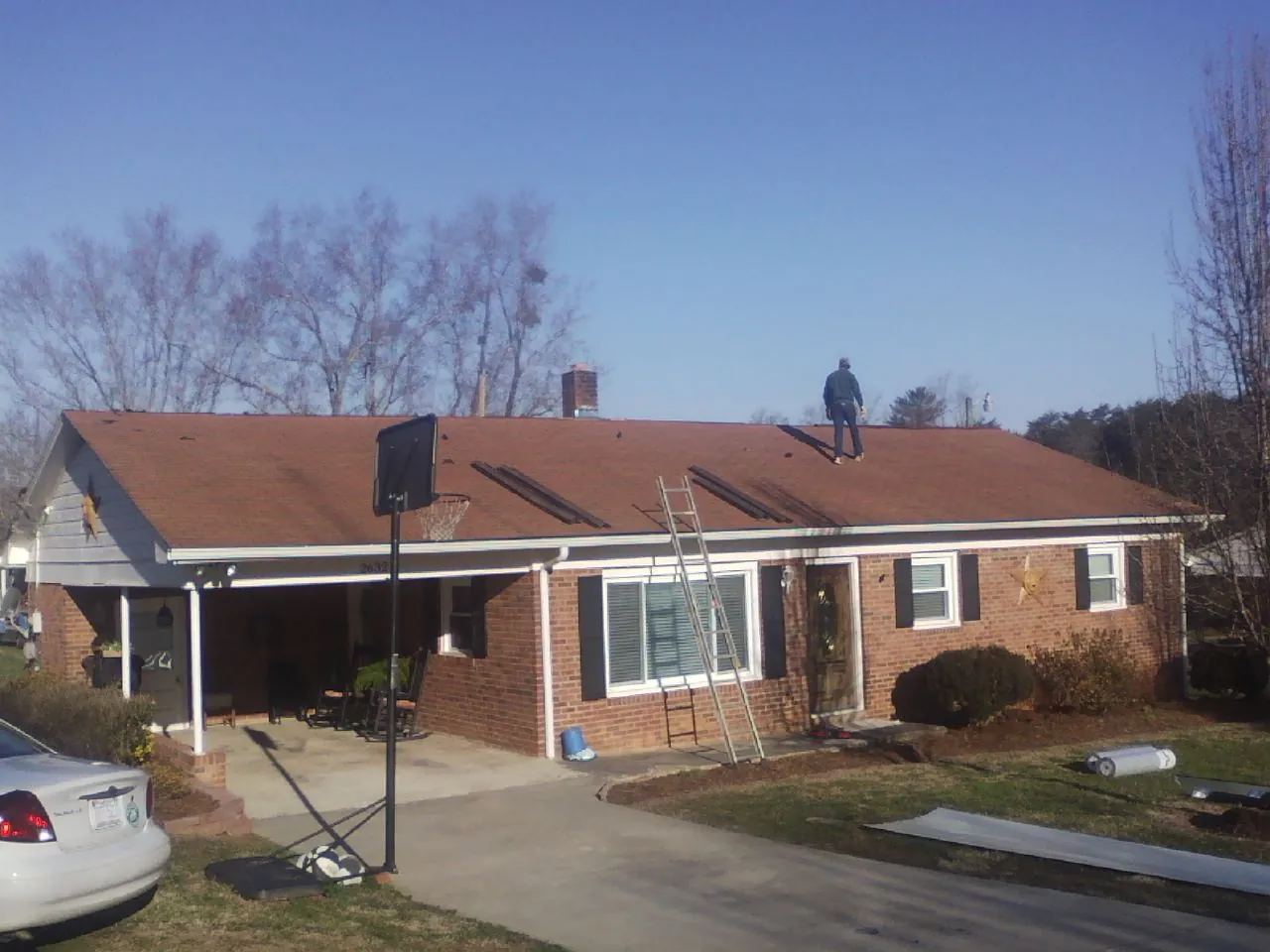 Roofer stripping a shingle roof on a brick ranch before metal panels in Henrietta