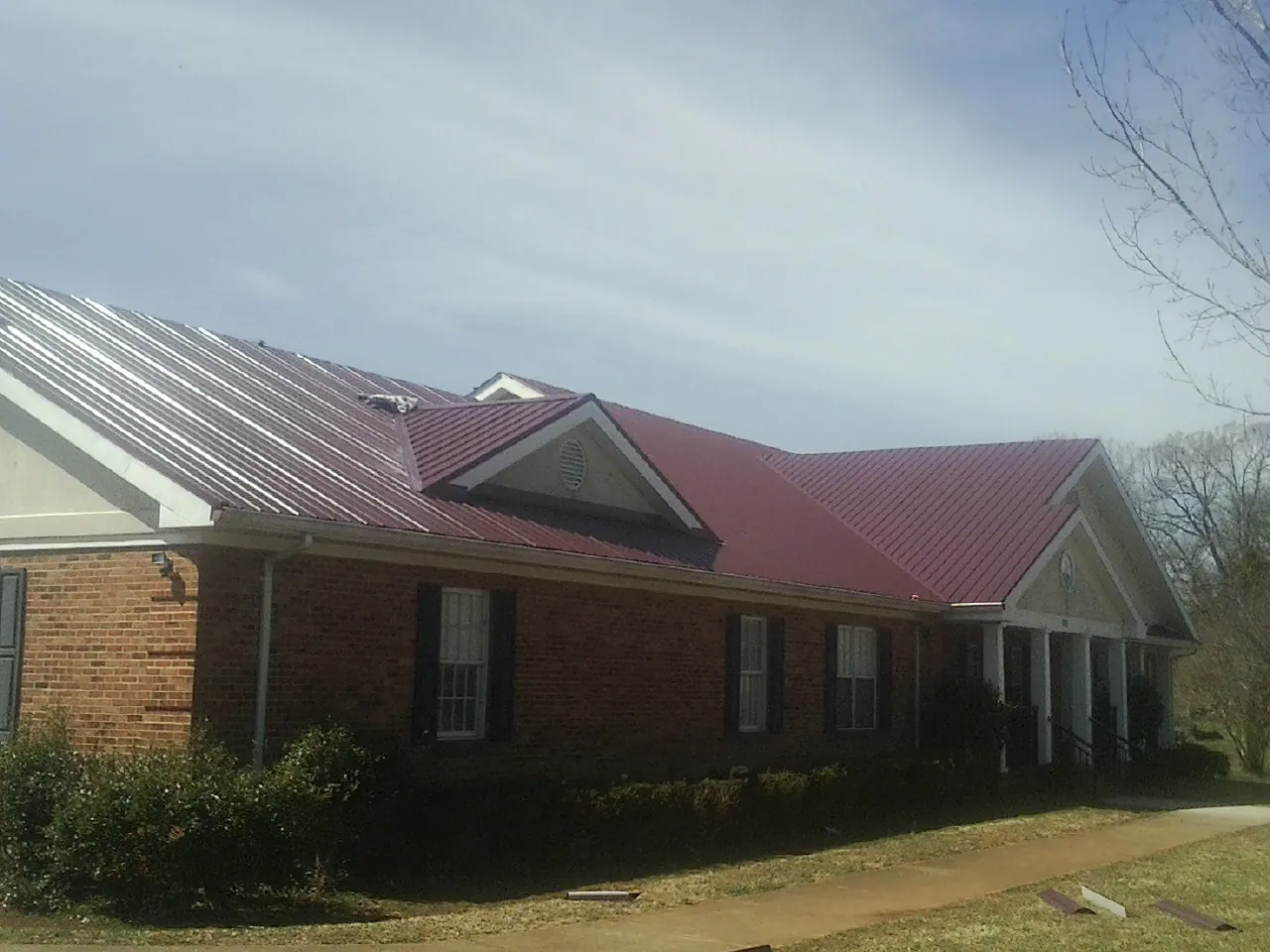 Red metal roof with gabled entries on a long brick building, from a Hail Damage Roof Repair job in Henrietta