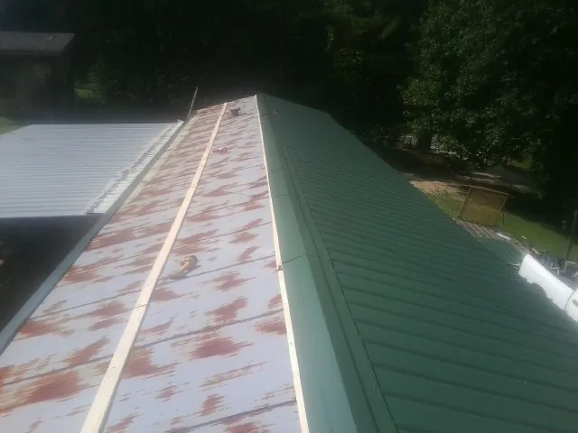 Old rusted panels beside newly installed green metal roofing — Wind Damage Roof Repair by Roofing Brothers in Henrietta
