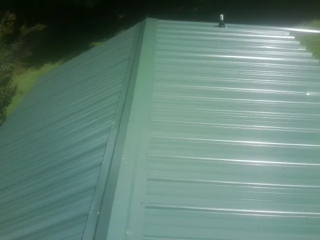 New green metal panels meeting at the ridge of a roof — Flat Roof Repair work by our crew in Henrietta