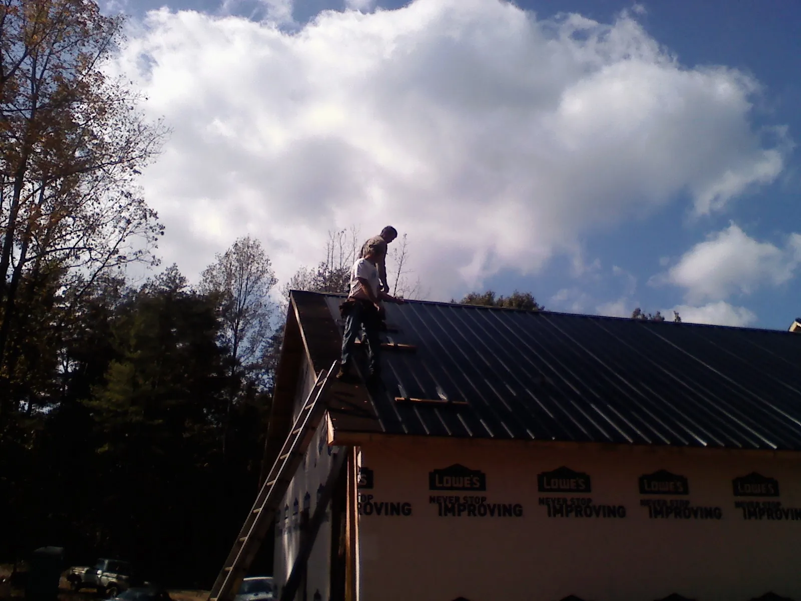 Roofer fastening dark metal panels high against a cloudy sky, from a Roof Inspection job in Henrietta